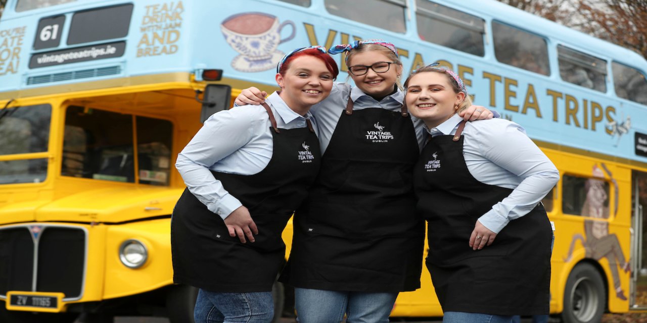 3 colleagues posing infront of blue and yellow bus 